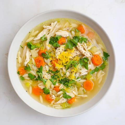 Frisch gekochte Lemon Pepper Chicken Orzo Soup in einer Hellblau-glasurten Keramikschüssel, dampfend serviert mit zitroniger Note und schwarzem Pfeffer.