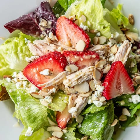 Frische Strawberry Poppy Seed Chicken Salad mit zartem Hähnchen, Erdbeeren und knusprigen Mandeln auf grünem Salat.